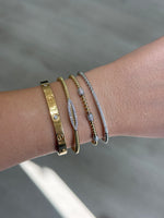 Load image into Gallery viewer, Close-up of a wrist wearing multiple gold and white gold bracelets on a neutral background