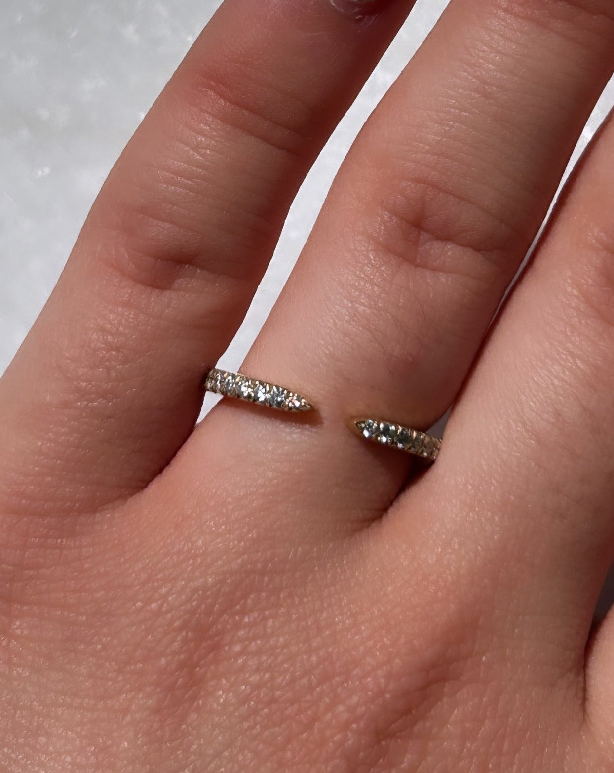 Image showing a yellow gold diamond band on a hand against a marble background. The hand moves, highlighting the shimmer of the diamonds.