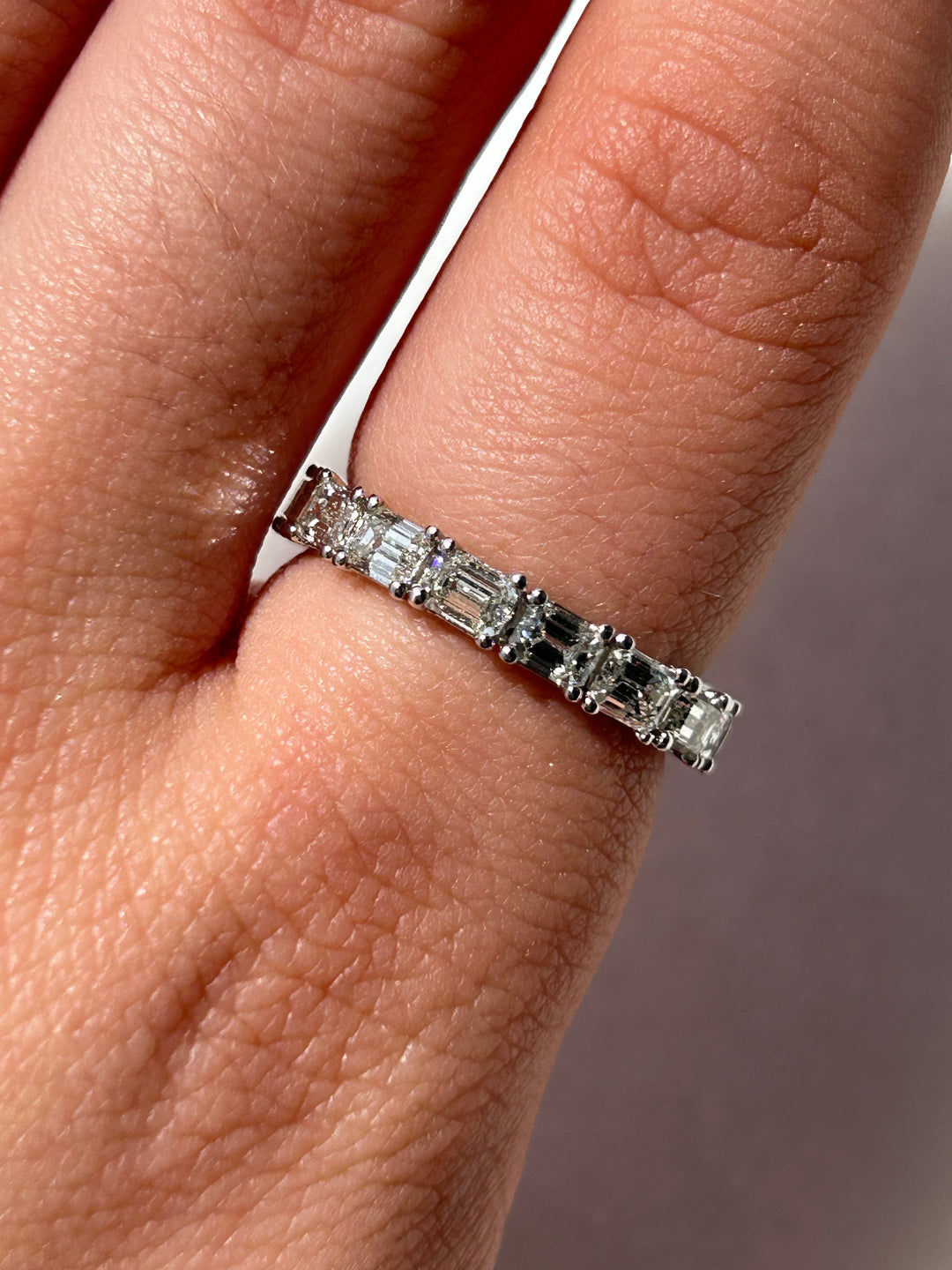 More close up image featuring a model elegantly displaying an emerald diamond eternity band, the sparkling emerald-cut diamonds intricately set around the band, catching the light with mesmerizing brilliance as the model's hand moves gracefully, showcasing the luxurious and timeless beauty of the jewelry piece against a subtle background.