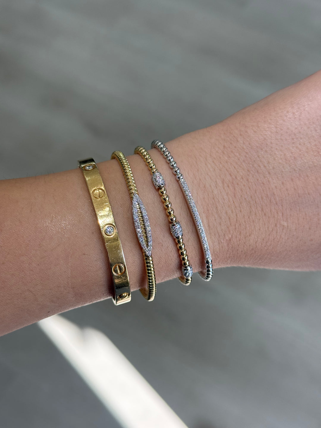 Close-up of a wrist wearing multiple gold and white gold bracelets on a neutral background