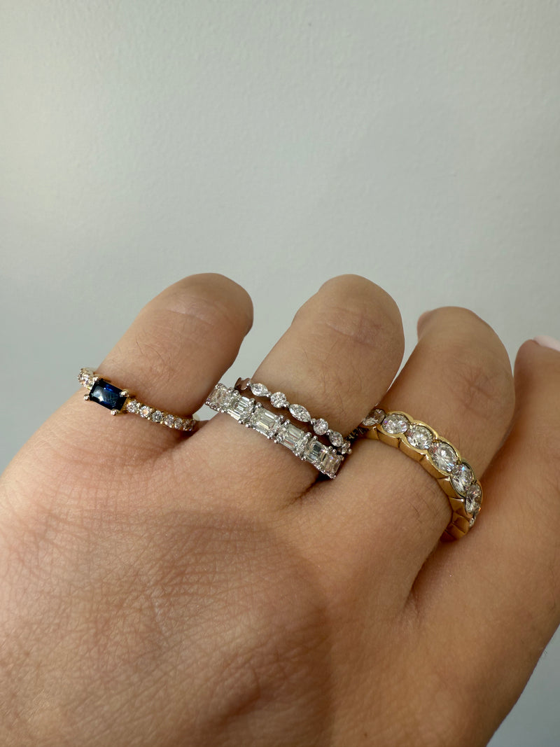 Hand wearing three rings with gemstones on a neutral background